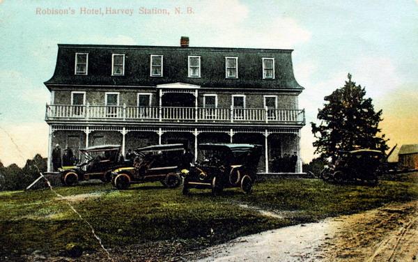 A postcard of &#039;Robison&#039;s Hotel, Harvey Station, N.B.&#039; with guests seated on the veranda and several early automobiles parked on the lawn out front iy was photographed around 1910. Image courtesy of J. Hall.