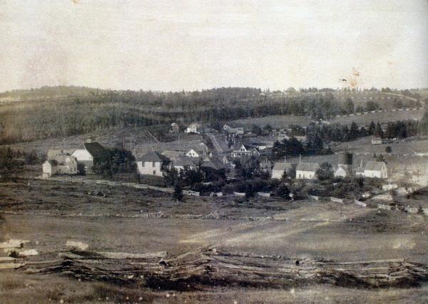 Postcard of village of Harvey Station taken from northwest. Steeple of St. James Presbyterian Church is not present so image was taken brfore 1897 the year the church was completed. Cedar rail &#039;snake fences&#039; a very typical fencing style in the Harvey area in foreground. Image thanks to J. Hall.